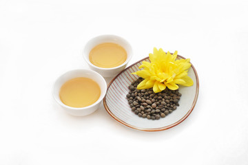 Obraz na płótnie Canvas Скрученные чайные листья женьшеня на белом блюдце с желтым цветком с двумя маленькими чашками зеленого чая