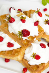waffles with wild strawberries and whipped cream on white table