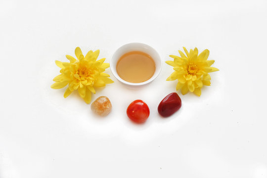 Белая пиала с зеленым чаем рядом с самоцветами: сердолик, цитрин, красный агат и две желтые хризантемы