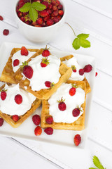 waffles with wild strawberries and whipped cream on white table