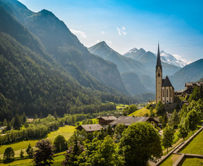 Rural landscape of Heiligenblut with St Vincent Church in Carynthia and Grossglockner (3797 m. elevation) highest mountain from Austria in background. - obrazy, fototapety, plakaty