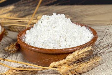 Wheat spikes beside a pottery bowl with pastry flour. Staple foods.