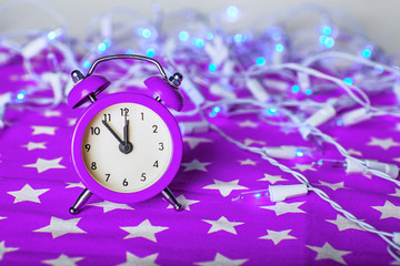 purple alarm clock with lights bokeh on a violet fabric backgrou