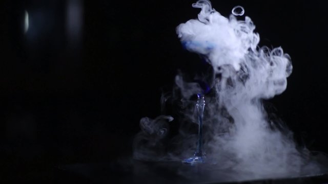 beautiful magical potion in a glass with a blue drink and steam, bubbling elegant delicious  cocktail on a black background