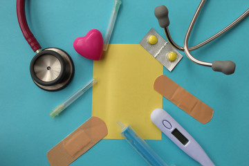 Medical theme -pill, syringe, needle, medical thermometer, bandage, sthetoscope and sticky note - copy space on blue background