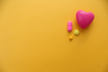 Obraz premium Pill and heart - copy space - medical concept on yellow background