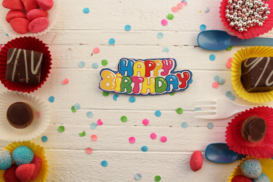 Birthday celebration cupcake, candy, plastic fork and spoon and confetti background
