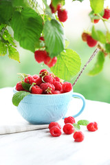 Fresh raspberries in cup on wooden table on blurred nature background