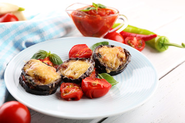 Dish of eggplant with cherry tomatoes and cheese in white plate on wooden table, closeup