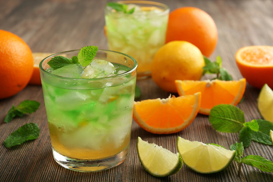 Glasses of lime juice with orange on wooden table, closeup