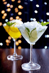 Glasses of cocktails with ice on blurred lights background
