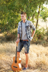 A handsome guy with a guitar standing in the forest