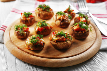 A wooden tablet with stuffed mushrooms on the table