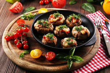 A frying pan with stuffed mushrooms and vegetables on the table