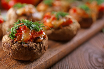 A wooden tablet with stuffed mushrooms and vegetables on the table, close-up