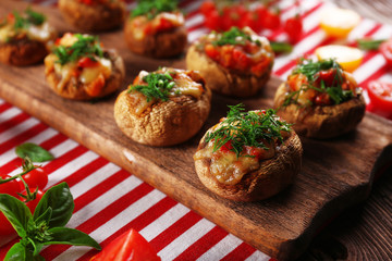 A wooden tablet with stuffed mushrooms and vegetables on the table
