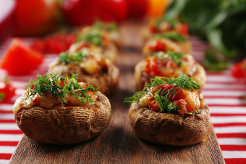 A wooden tablet with stuffed mushrooms and vegetables on the table
