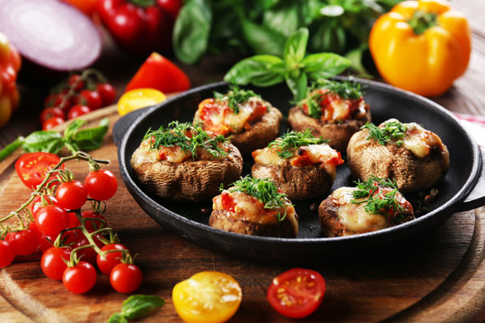 A frying pan with stuffed mushrooms and vegetables on the table