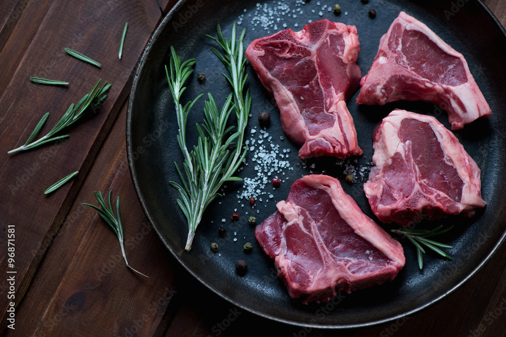 Sticker Raw T-bone lamb steaks with seasonings in a frying pan, close-up