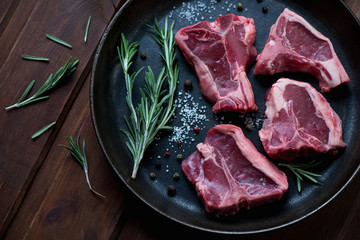 Raw T-bone lamb steaks with seasonings in a frying pan, close-up