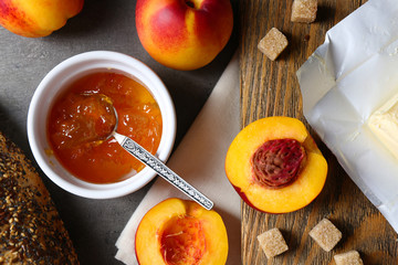 Tasty jam in the bowl, ripe peaches, butter, crackers and fresh bread on wooden tablet close-up