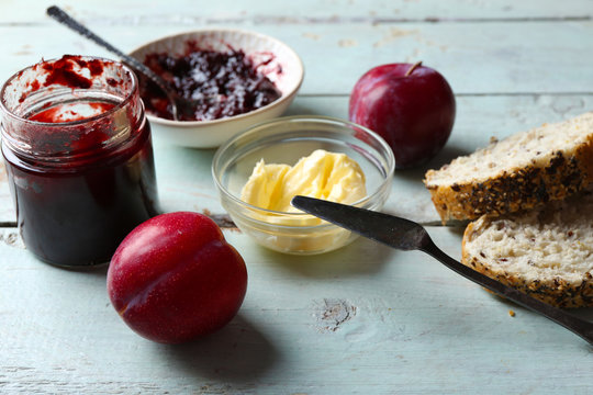Tasty jam in the jar and bowl, butter, fresh bread and plums on blue wooden background
