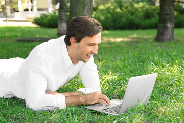 Man with laptop lying on green grass in the park