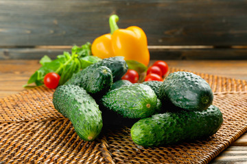 Composition of cucumbers, tomatoes and sweet peppers on wicker serviette against wooden background