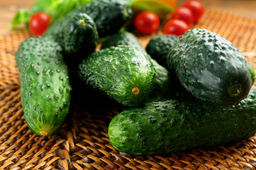 Composition of cucumbers, tomatoes and sweet peppers on wicker serviette against wooden background, close up