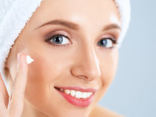 Beautiful young woman applying a creme on her face isolated on gray background