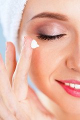 Beautiful young woman applying a creme on her face isolated on gray background