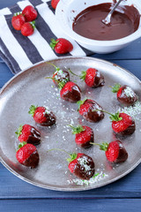 A plate of strawberries in chocolate on blue wooden background