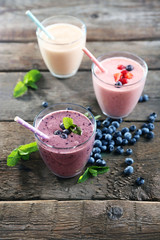 Tasty blueberry, strawberry and milk yogurts with berries and mint around on wooden background