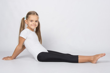 Fototapeta na wymiar Girl gymnast sitting on the floor with legs stretched and leaned back on his hands