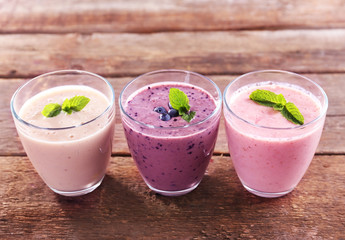 Tasty blueberry, strawberry and milk yogurts in a row on wooden background