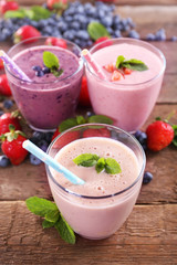 Tasty blueberry, strawberry and milk yogurts in a row decorated with berries and mint on wooden background, close up