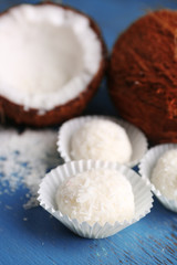Candies in coconut flakes and fresh coconut on color wooden background