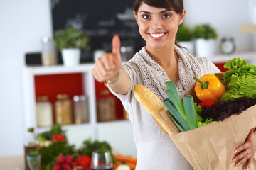 Young woman holding grocery shopping bag with vegetables Standing in the kitchen and showing ok