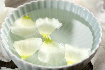 Flower petals in bowl with water on wooden background