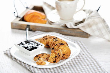 Plate of tasty cookies with chocolate crumbs and jam against cup of coffee on wooden tray