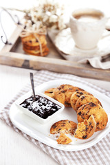 Plate of tasty cookies with chocolate crumbs and jam against cup of coffee on wooden tray