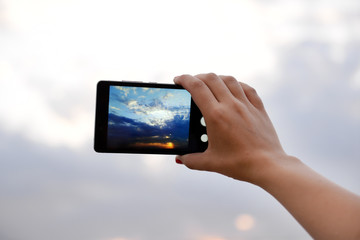 Woman using smart phone for taking photo of beautiful sky
