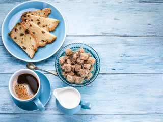 Cup of coffee, milk jug, cane sugar cubes and fruit-cake.