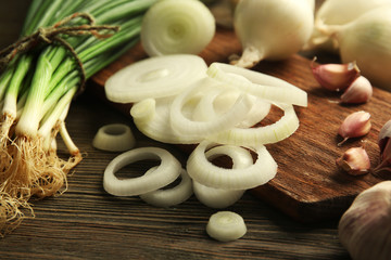 Onions circles, fresh green onion with garlic on board against wooden background