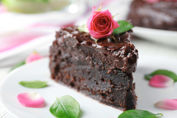 Piece of chocolate cake decorated with flowers on white wooden table