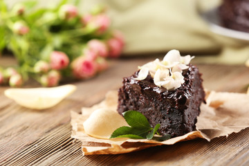 Piece of chocolate cake decorated with flowers on brown wooden table