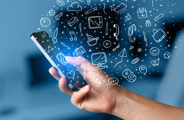 Hand holding smartphone with hand drawn media icons and symbols