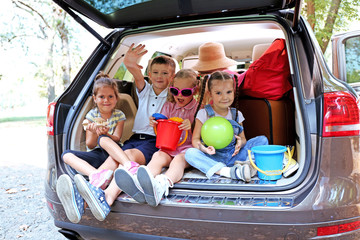 Three beautiful girls and boy sit on a car trunk and laughing