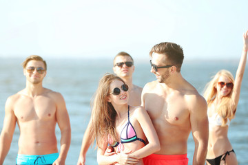 Fototapeta premium Happy couple and their playful friends relaxing at the beach, outdoors