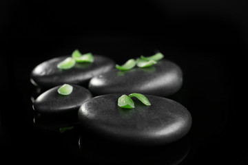 Stack of stones and green petals, on black background. Spa relaxation concept